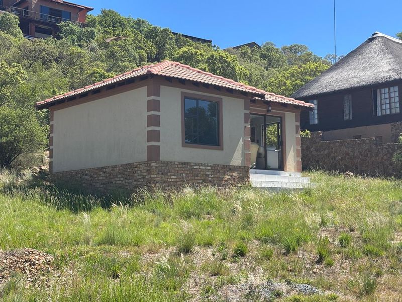 A detached outbuilding featuring a terracotta tile roof, brick base, and sliding glass door, situated on a sloped, natural landscape.