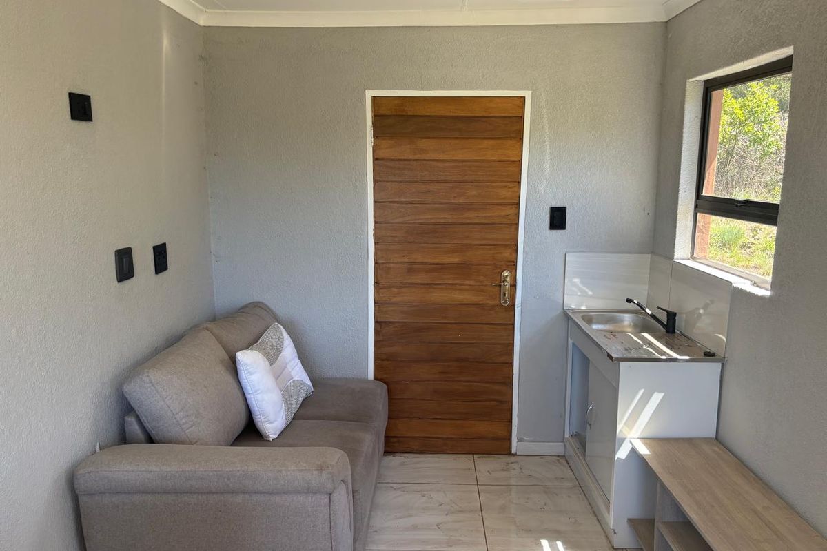 A compact kitchenette area featuring tiled flooring, a stainless steel sink, and a timber door, providing a functional space for basic food preparation.