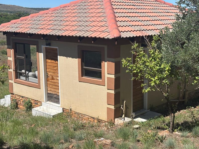 A rear view of a small detached structure featuring a tiled roof, timber doors, and aluminium window frames set against a natural landscape.