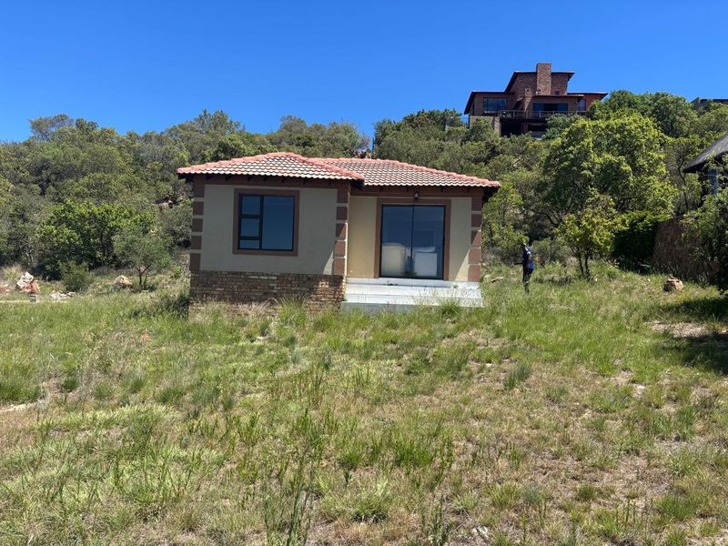 A detached single-story dwelling featuring a tiled roof, brick base detailing, and aluminium-framed windows and sliding doors, set within a natural landscape.