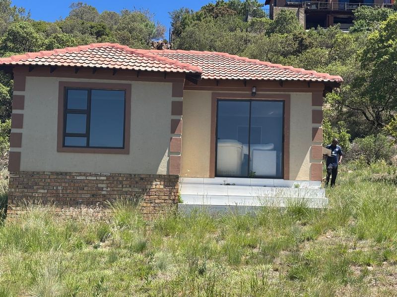 A single-story residential structure featuring a tiled roof, brick base, and sliding glass door entrance, situated on a sloped, grassed plot.