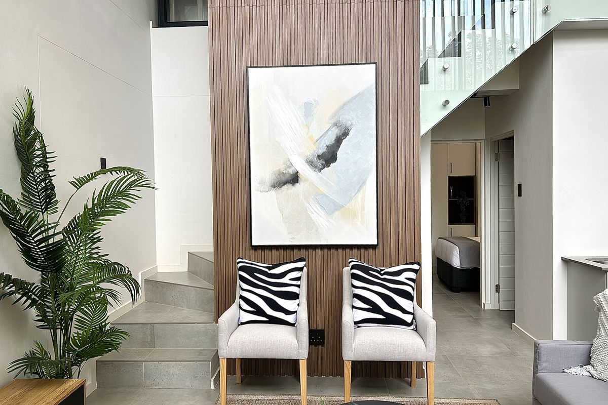 Modern living area featuring a striking vertical slatted timber feature wall, tiled flooring, and a contemporary staircase with a glass balustrade.