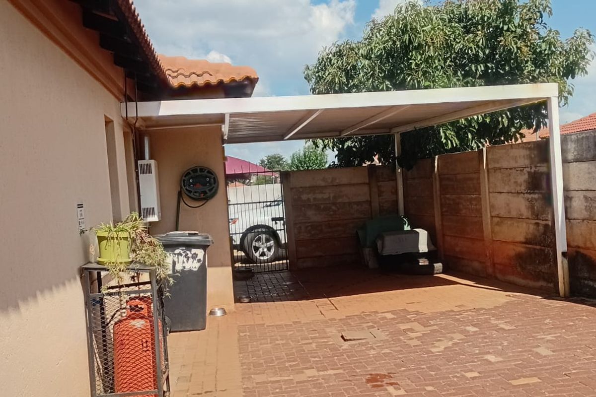 A paved outdoor area featuring a covered carport structure and a high boundary wall, providing a functional space for vehicle parking or storage.