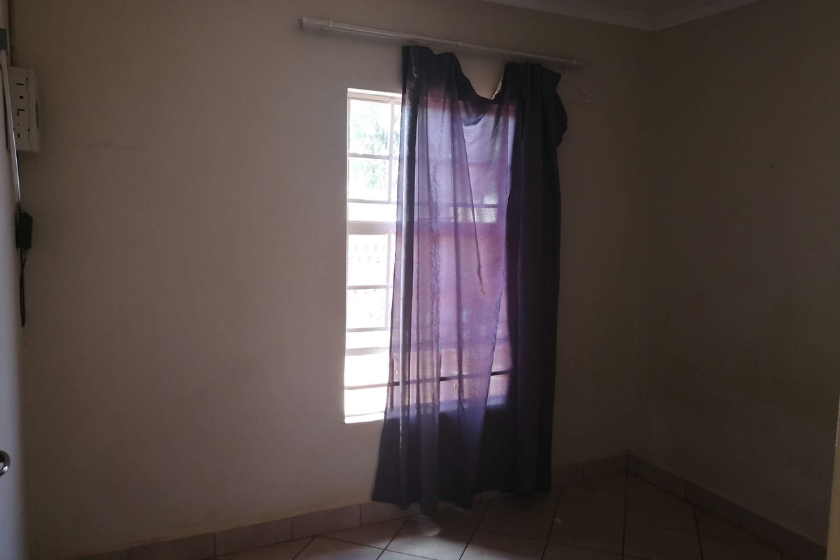 A vacant bedroom featuring tiled flooring and a window fitted with security bars, offering a blank canvas for potential interior design updates.