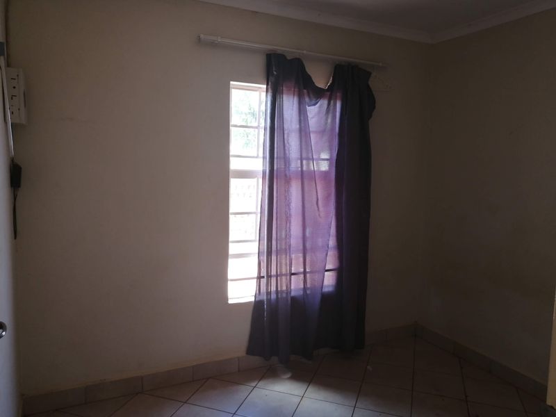 A vacant bedroom featuring tiled flooring and a window fitted with security bars, offering a blank canvas for potential interior design updates.