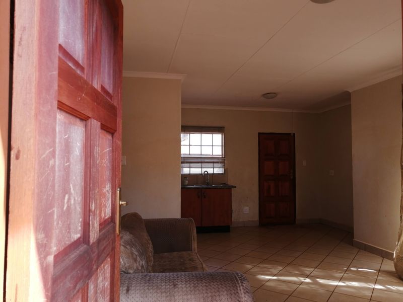Open plan living area featuring tiled flooring, a small kitchen kitchenette with sink, and wooden panel doors.
