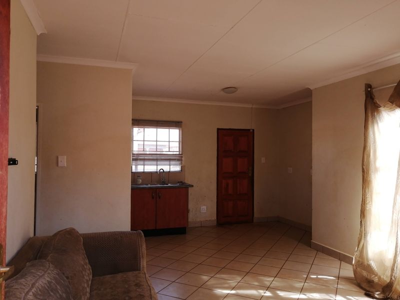 Open plan living area featuring tiled flooring, a small kitchenette with sink, and access to a timber door.