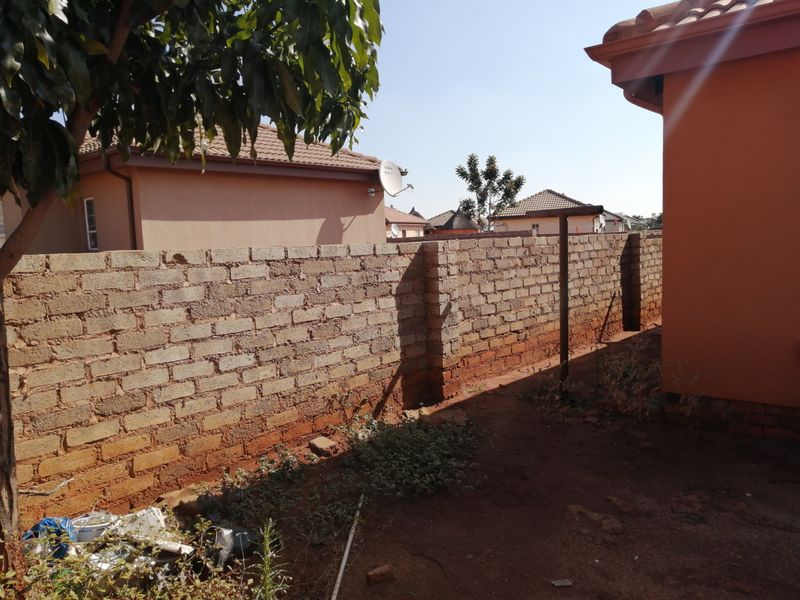A view of the rear exterior area featuring an unfinished perimeter brick wall and tiled roof structure.