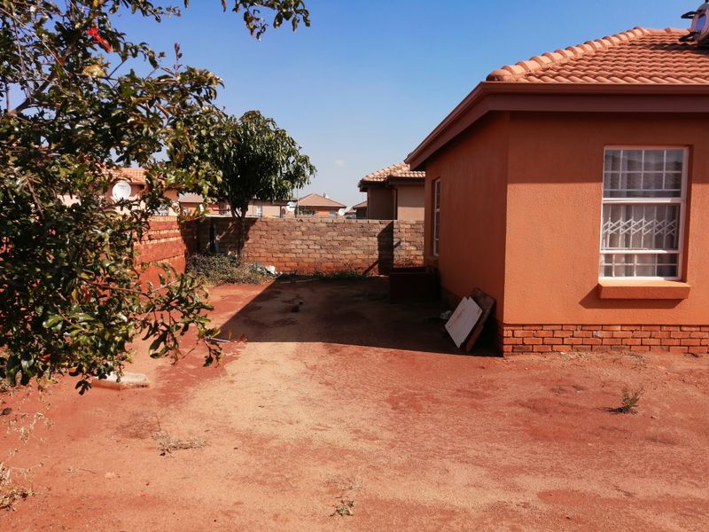 Rear exterior view of the property featuring a tiled roof, plastered walls, security bars on windows, and an open, unlandscaped backyard area.