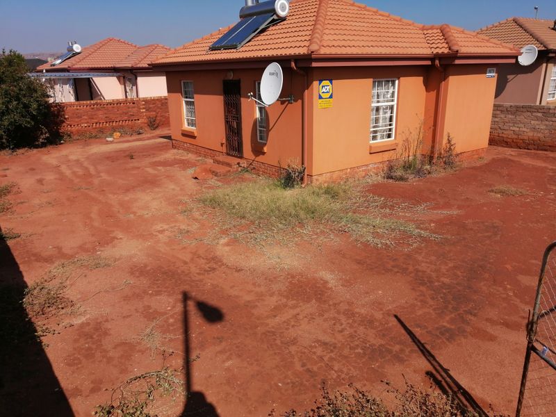 Rear view of a detached house featuring a tiled roof, solar water heater, and a large, unlandscaped yard area.