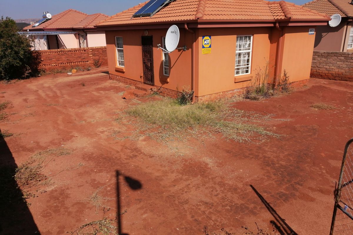 Rear view of a detached house featuring a tiled roof, solar water heater, and a large, unlandscaped yard area.
