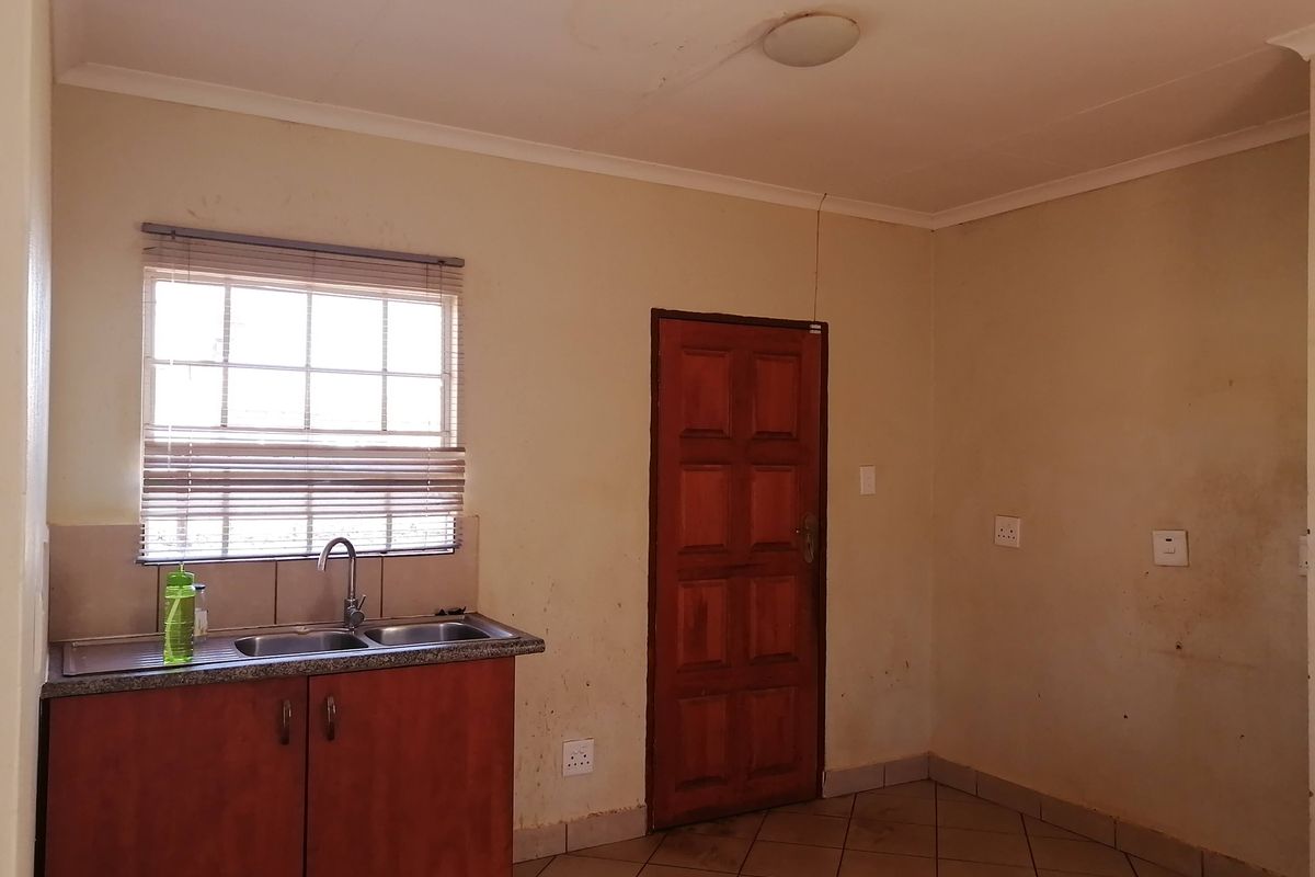 A compact kitchen area featuring basic base cabinetry, a stainless steel sink, tiled flooring, and a window with blinds, requiring cosmetic updates.
