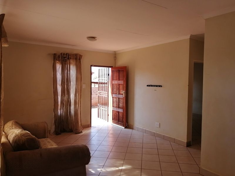 A living room featuring tiled flooring, a timber entrance door with a security gate, and a wall-mounted television bracket.