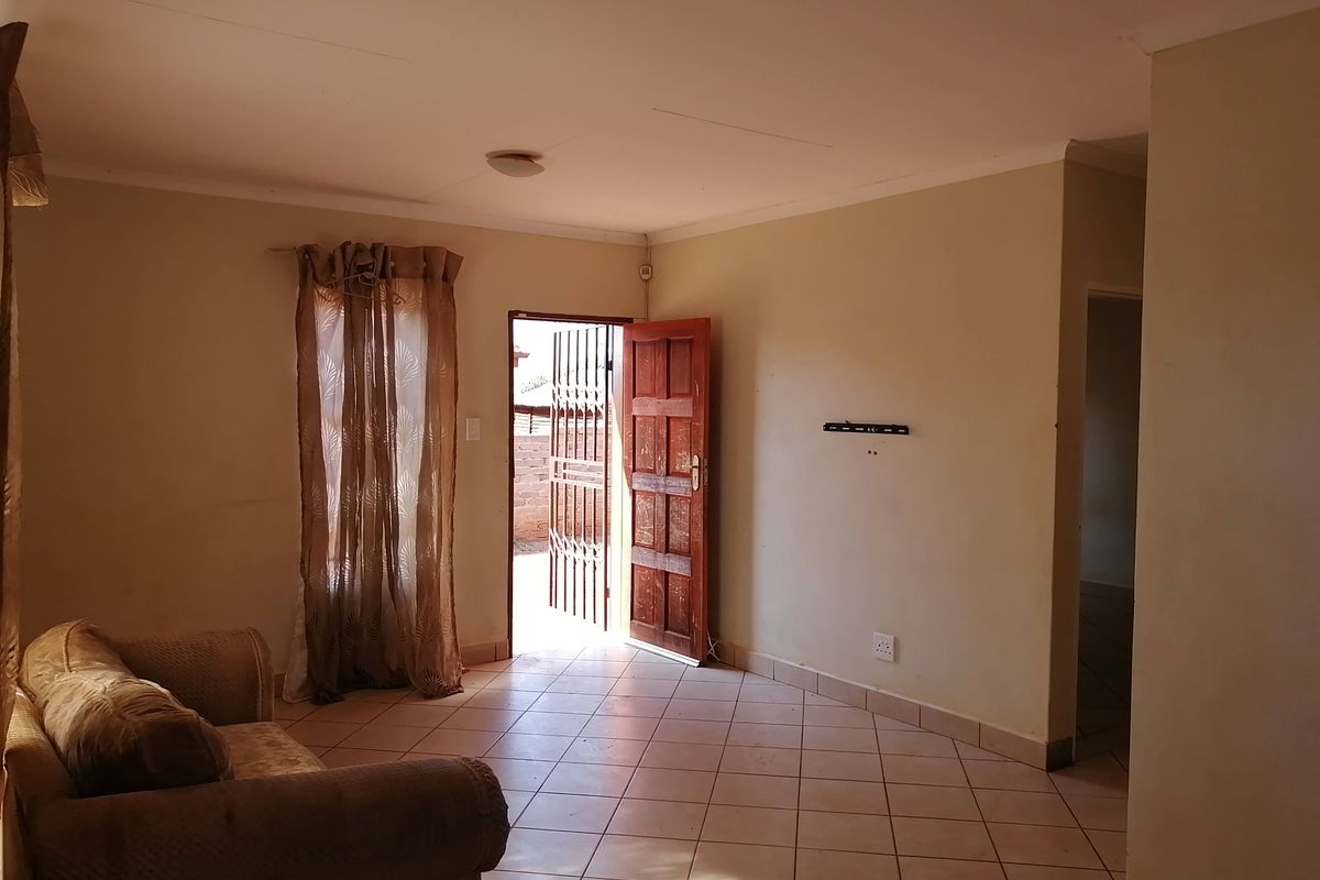 A living room featuring tiled flooring, a timber entrance door with a security gate, and a wall-mounted television bracket.