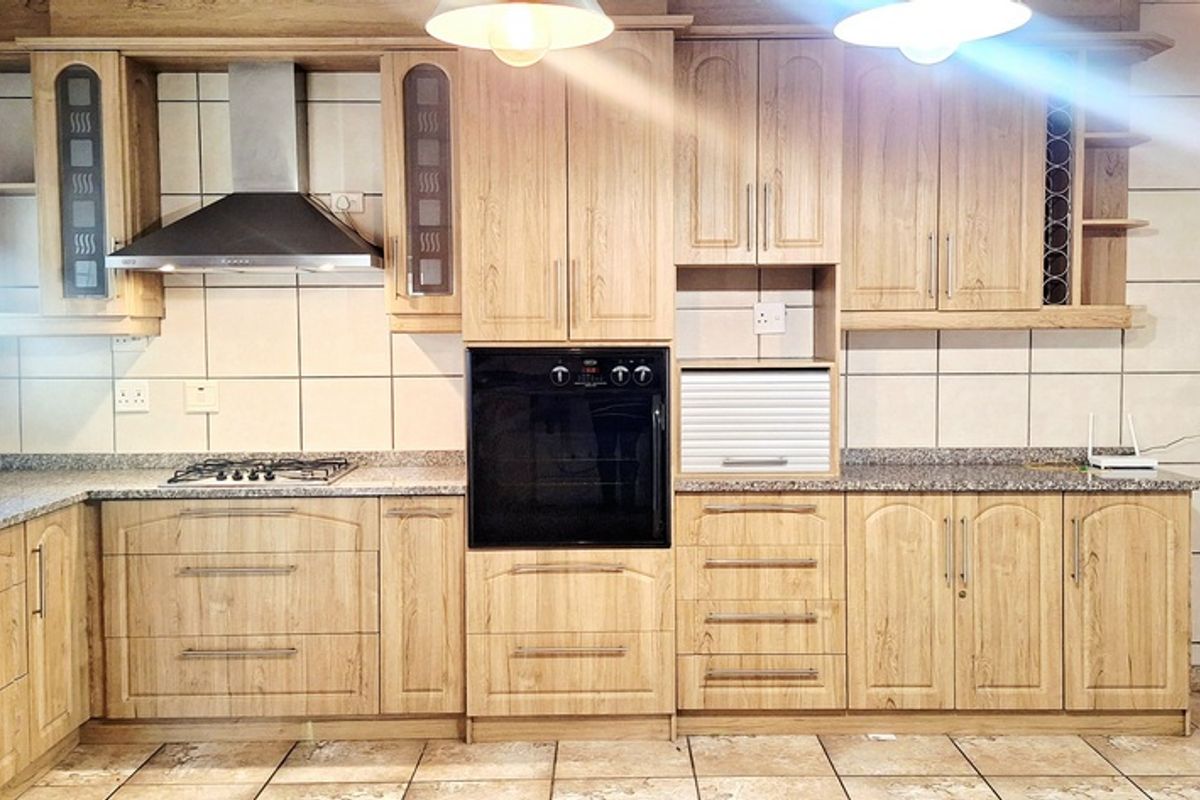 A functional kitchen featuring light wood-grain cabinetry, granite countertops, a built-in oven, gas hob, and stainless steel extractor fan with tiled splashbacks.