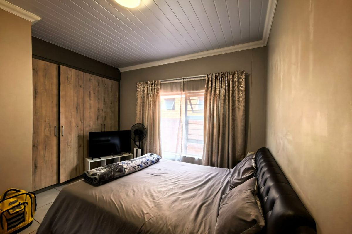 A bedroom featuring built-in wooden cupboards, a tongue-and-groove ceiling, and tiled flooring, providing a functional and comfortable living space.