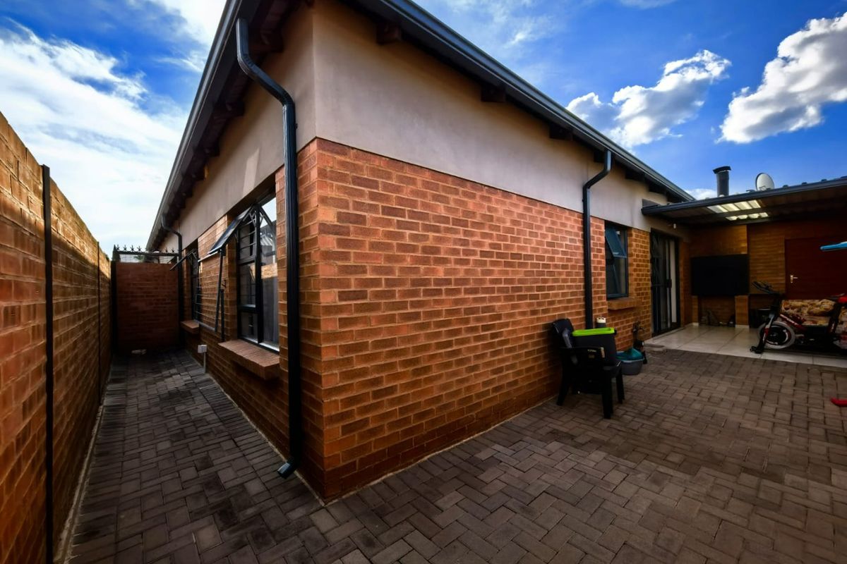 Rear exterior view of the townhouse featuring a paved patio area, brick facade, and covered outdoor space.