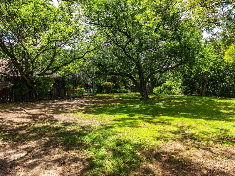 A spacious, shaded garden area featuring mature trees, established lawn, and perimeter fencing, offering a peaceful outdoor setting on the farm property.