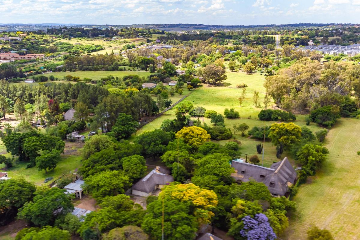 An aerial view of a farm property featuring multiple structures with thatched roofs, a swimming pool, and extensive surrounding green landscape.