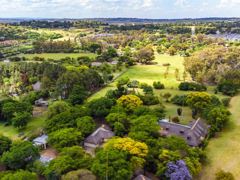 An aerial view of a farm property featuring multiple structures with thatched roofs, a swimming pool, and extensive surrounding green landscape.