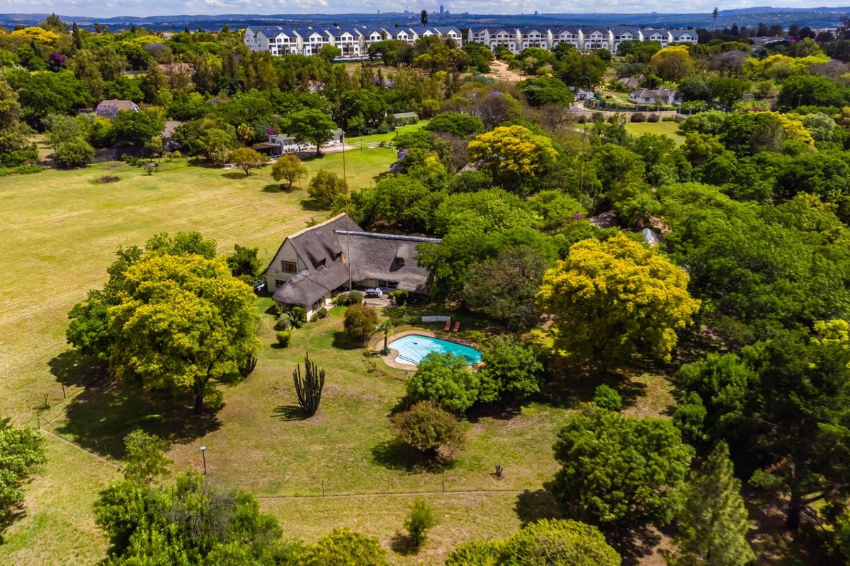 Aerial view of a farm property featuring a main residence with a thatched roof, a swimming pool, and extensive landscaped grounds.