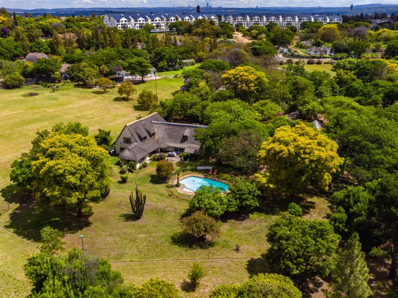 Aerial view of a farm property featuring a main residence with a thatched roof, a swimming pool, and extensive landscaped grounds.