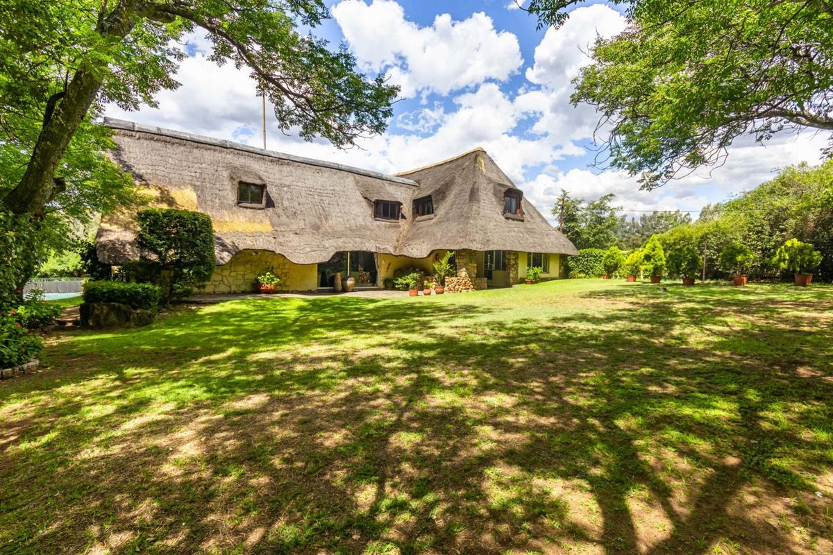 A rear view of a traditional farmhouse featuring a distinctive thatched roof, stone exterior walls, and a spacious, well-maintained garden setting.