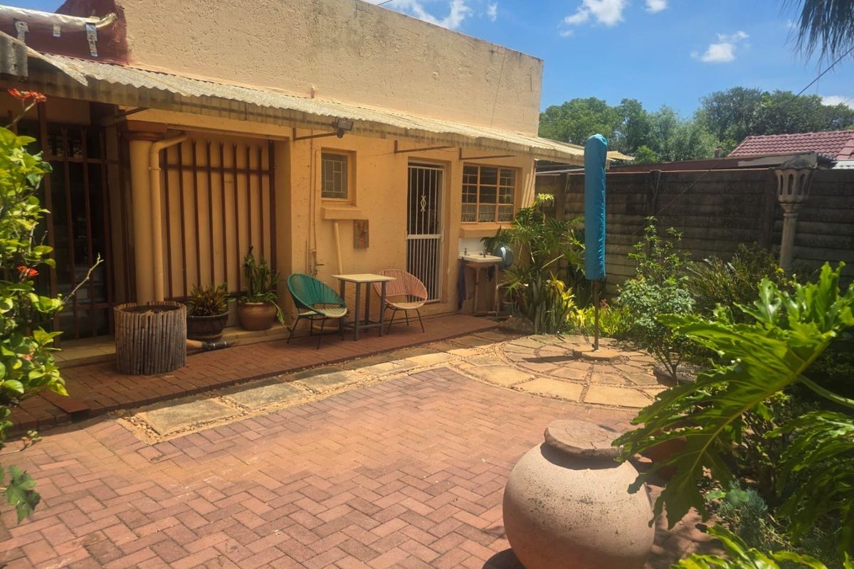 A rear exterior view of the property featuring a paved patio area, covered walkway, and established garden space.