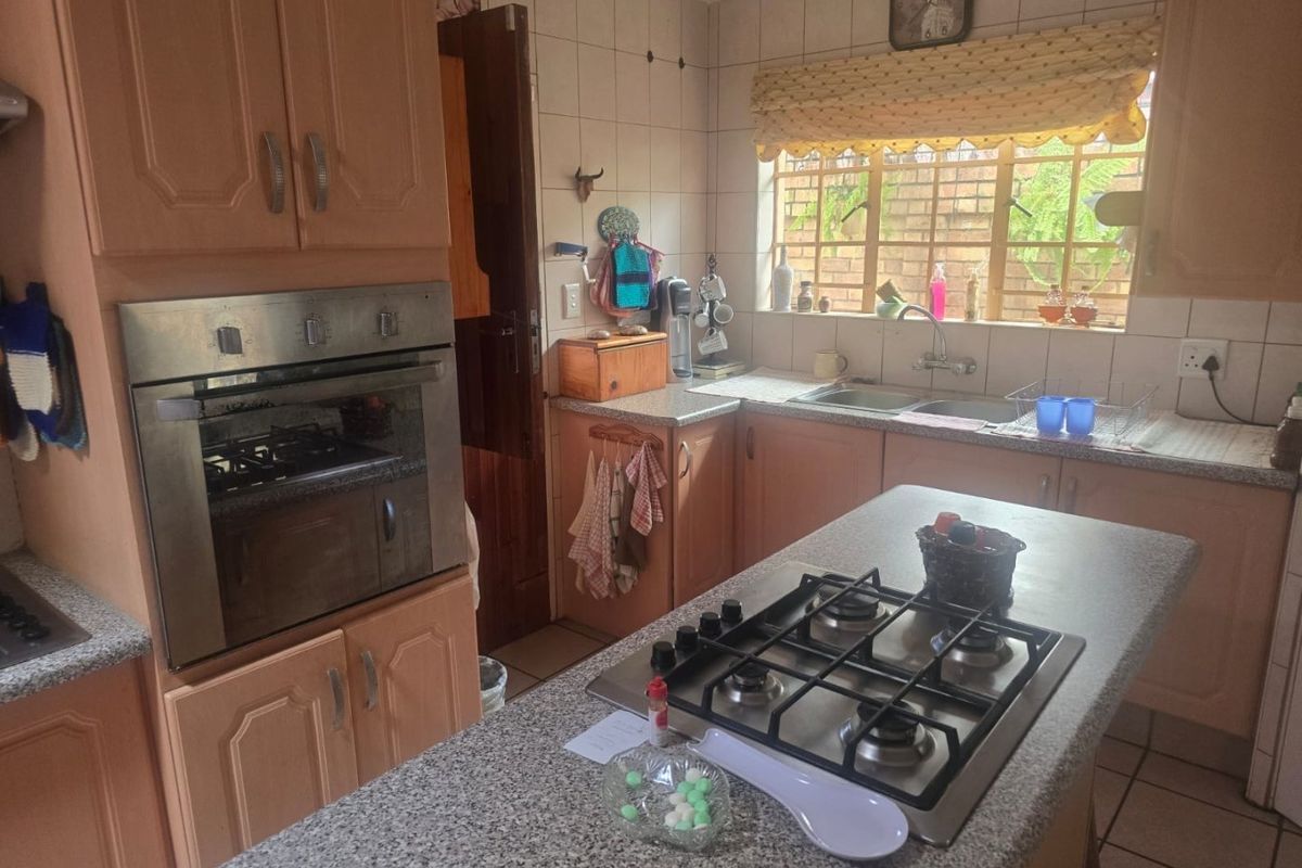 A functional kitchen featuring a central island with a built-in gas hob, wall-mounted oven, tiled splashbacks, and ample wooden cabinetry.