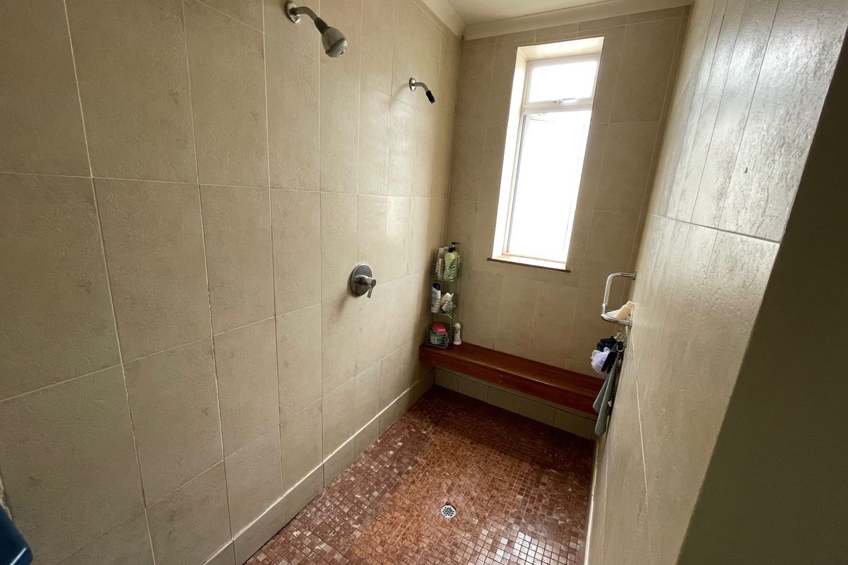A walk-in shower area featuring beige wall tiles, a mosaic tiled floor, a built-in wooden bench, and dual shower heads.