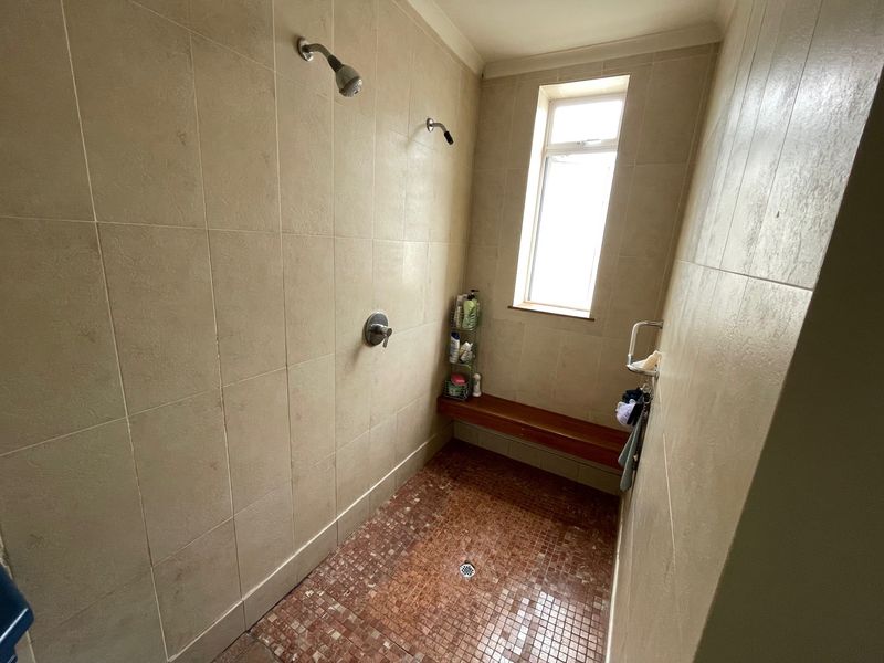 A walk-in shower area featuring beige wall tiles, a mosaic tiled floor, a built-in wooden bench, and dual shower heads.