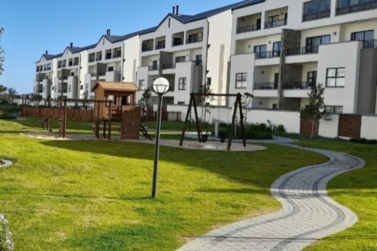 Exterior view of the apartment complex featuring a landscaped garden, paved walkways, and a communal children's play area.