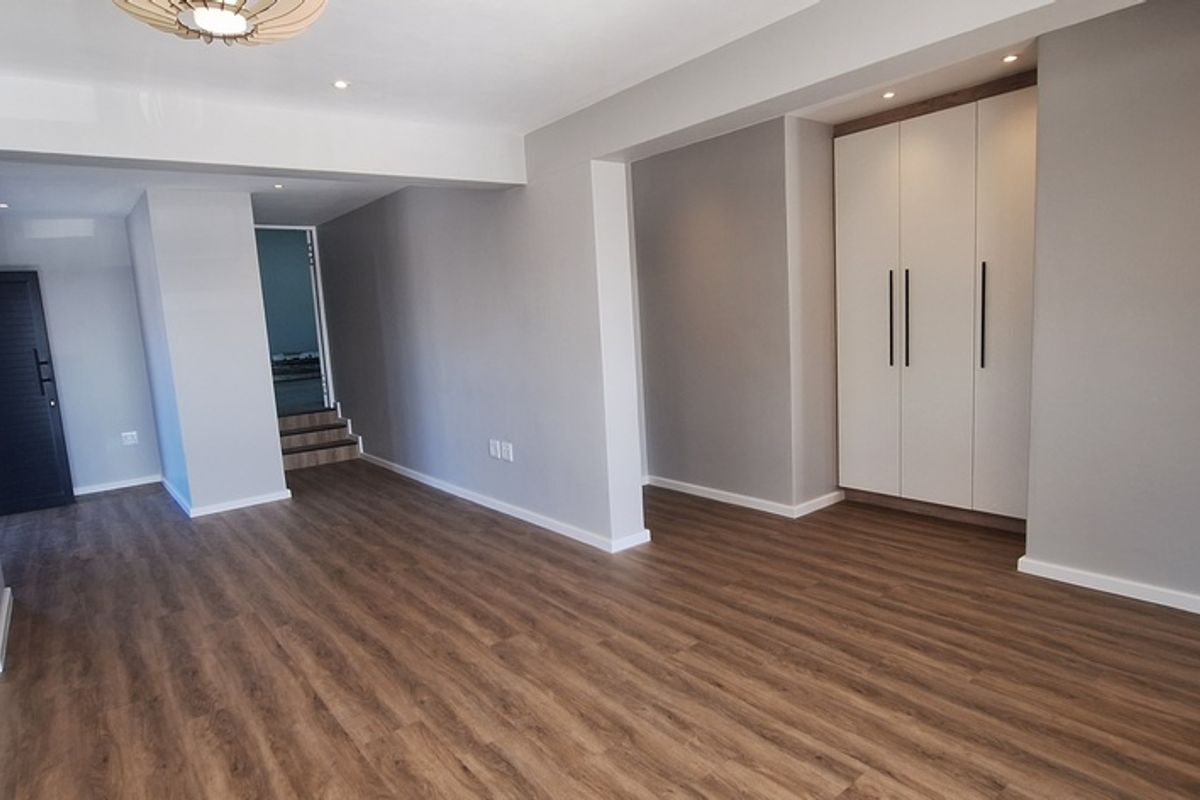 Spacious living area featuring modern wood-look flooring, recessed ceiling lighting, and built-in floor-to-ceiling cabinetry with a clean, contemporary finish.