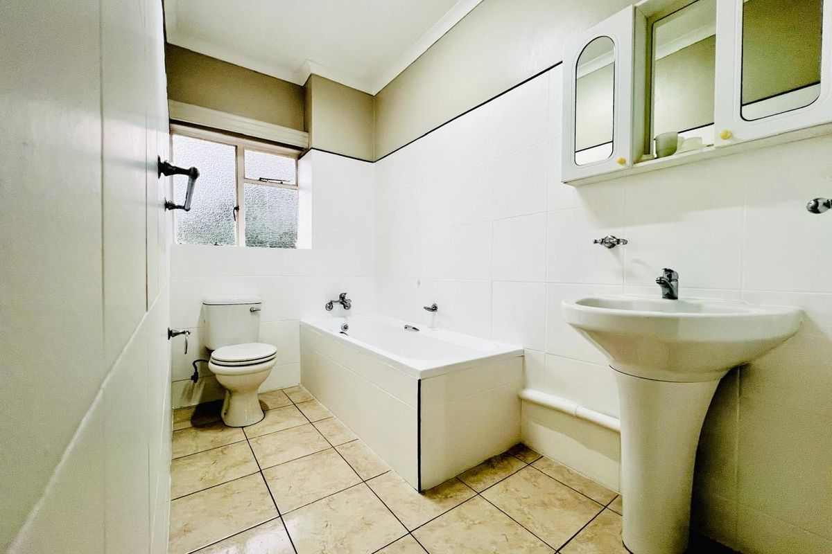 A functional bathroom featuring a white bathtub, pedestal basin, wall-mounted medicine cabinet, and tiled flooring.