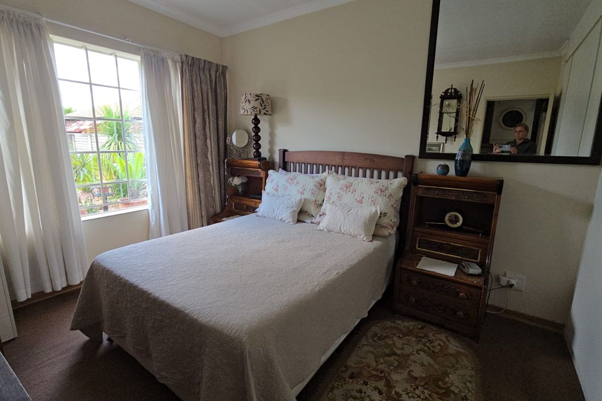A cozy bedroom featuring a large window with natural light, built-in cupboards, and a wall-mounted mirror.