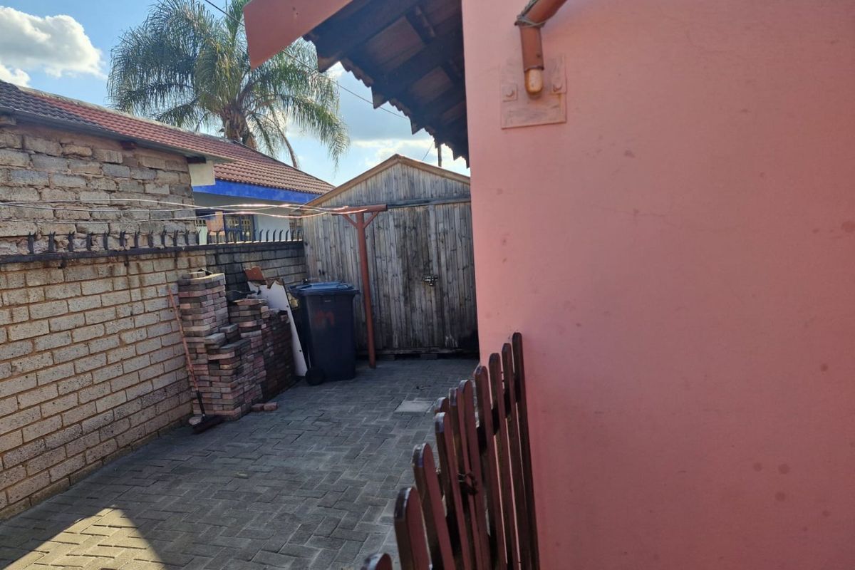 A side exterior area featuring paved ground, a brick boundary wall with metal spikes, and a weathered wooden storage shed.