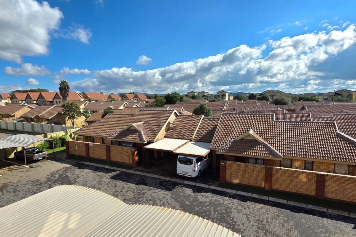 An elevated aerial view of a residential apartment complex featuring brick facades, tiled roofs, and covered parking bays within a secure estate setting.