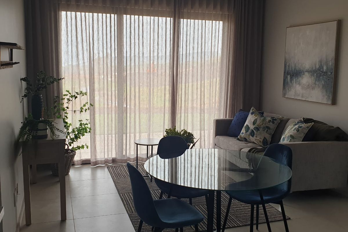 A bright living area featuring large sliding glass doors with floor-to-ceiling curtains and neutral tiled flooring.