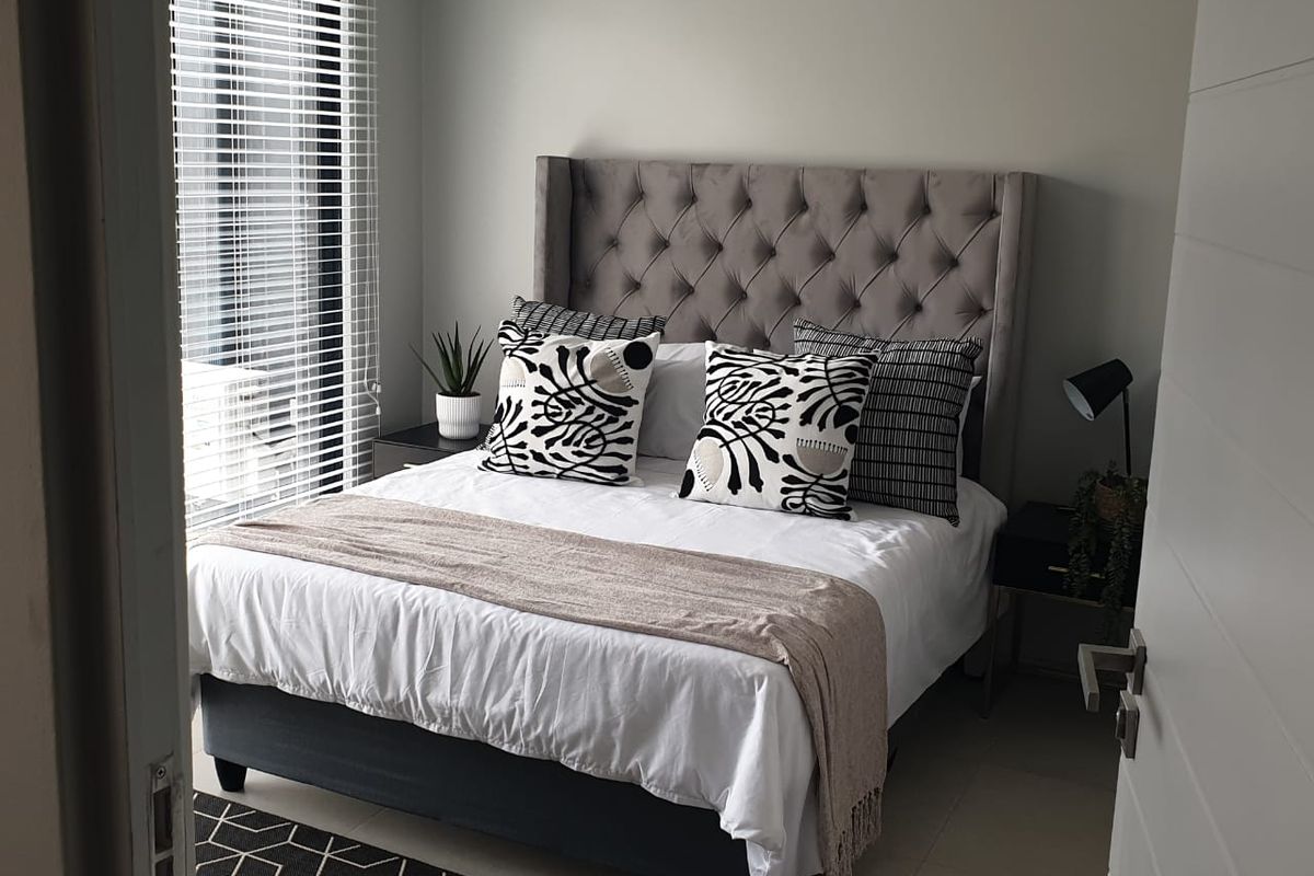 A well-maintained bedroom featuring neutral wall tones, tiled flooring, and large windows fitted with venetian blinds for natural light control.