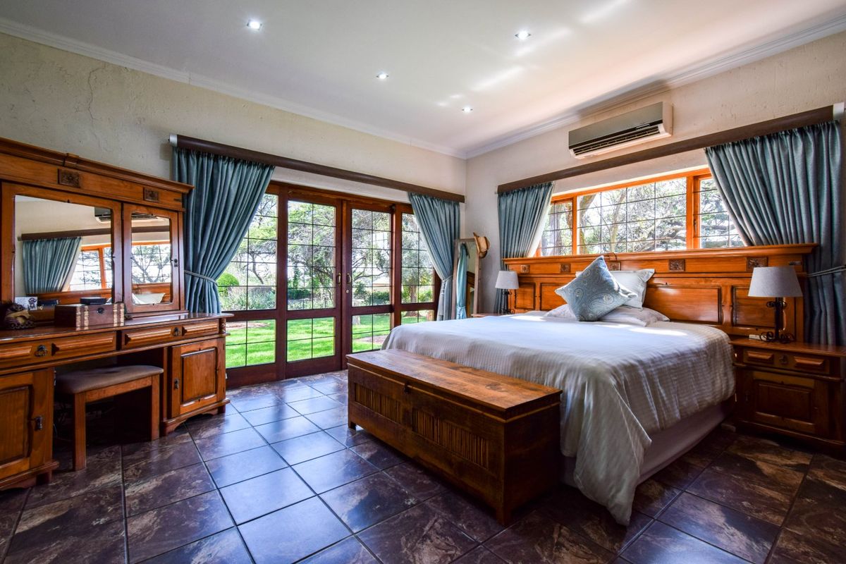Spacious bedroom featuring tiled flooring, built-in wooden headboard, recessed ceiling lighting, and large glass sliding doors providing direct access to the garden.