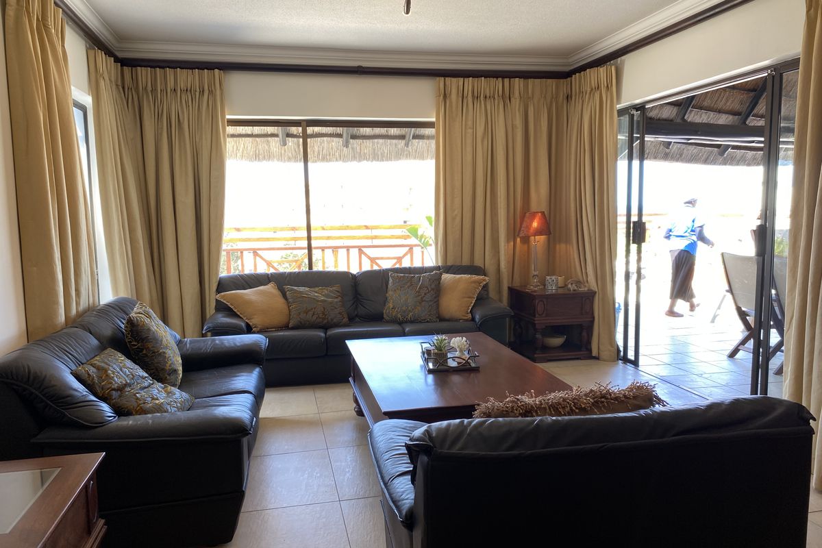 A comfortable living room featuring tiled flooring, crown molding, and large sliding glass doors that provide seamless access to an outdoor patio area.