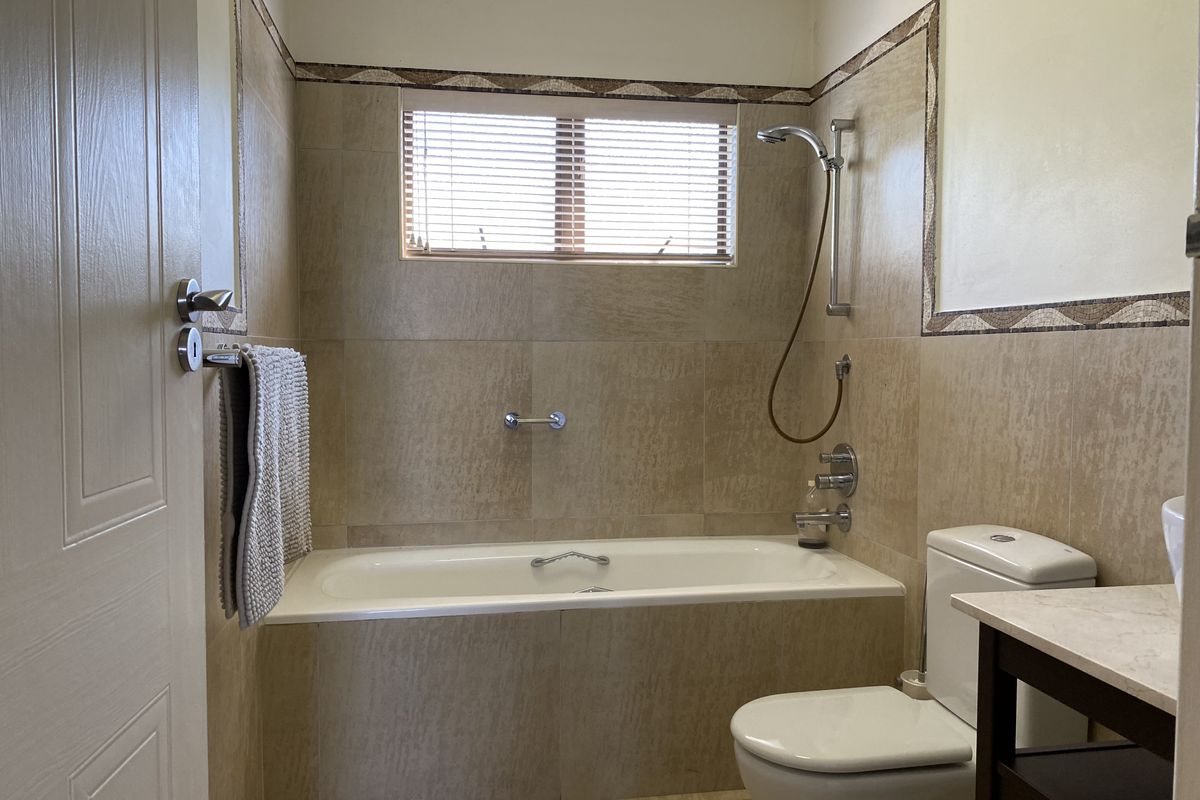 A functional bathroom featuring a built-in bathtub with shower mixer, tiled walls with decorative border, and a modern toilet.