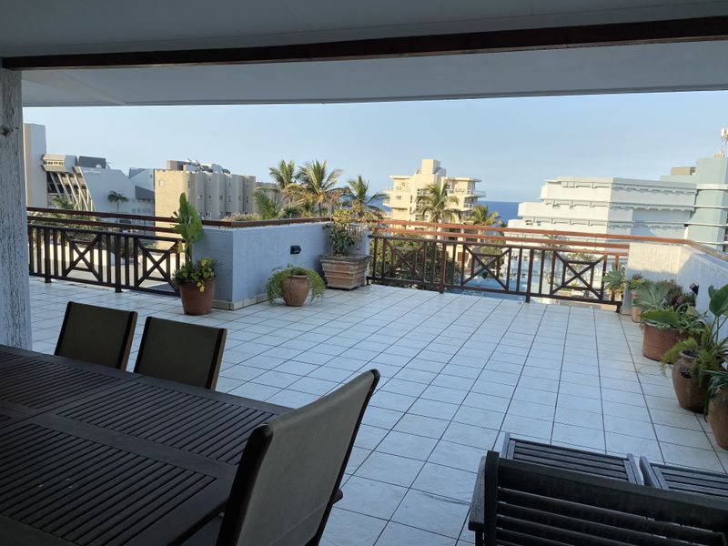 Spacious covered balcony featuring tiled flooring and a timber balustrade, offering an open-air outdoor living space with urban and partial sea views.