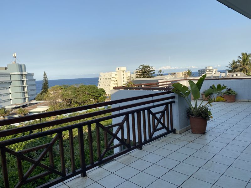 Spacious balcony featuring tiled flooring and a wooden balustrade, offering expansive views of the surrounding coastal area and ocean.