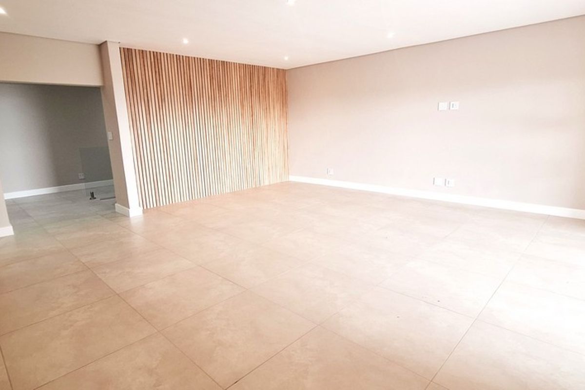 A spacious, empty living area featuring modern large-format floor tiles and a decorative timber slat feature wall.