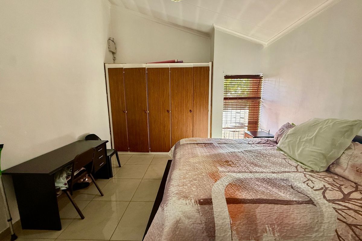 A bedroom featuring tiled flooring, a vaulted ceiling, and built-in wooden wardrobes with a window fitted with blinds.