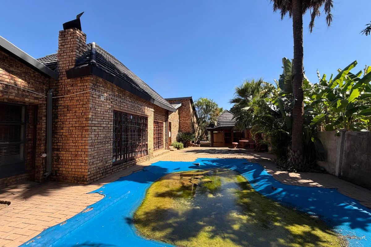Rear exterior view featuring a brick house facade, paved patio area, and a swimming pool covered with a heavily soiled safety cover.