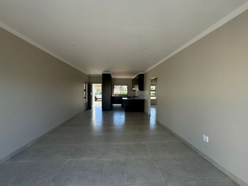 Spacious open-plan living area featuring neutral walls, tiled flooring, and a modern kitchen with dark cabinetry and a central island.