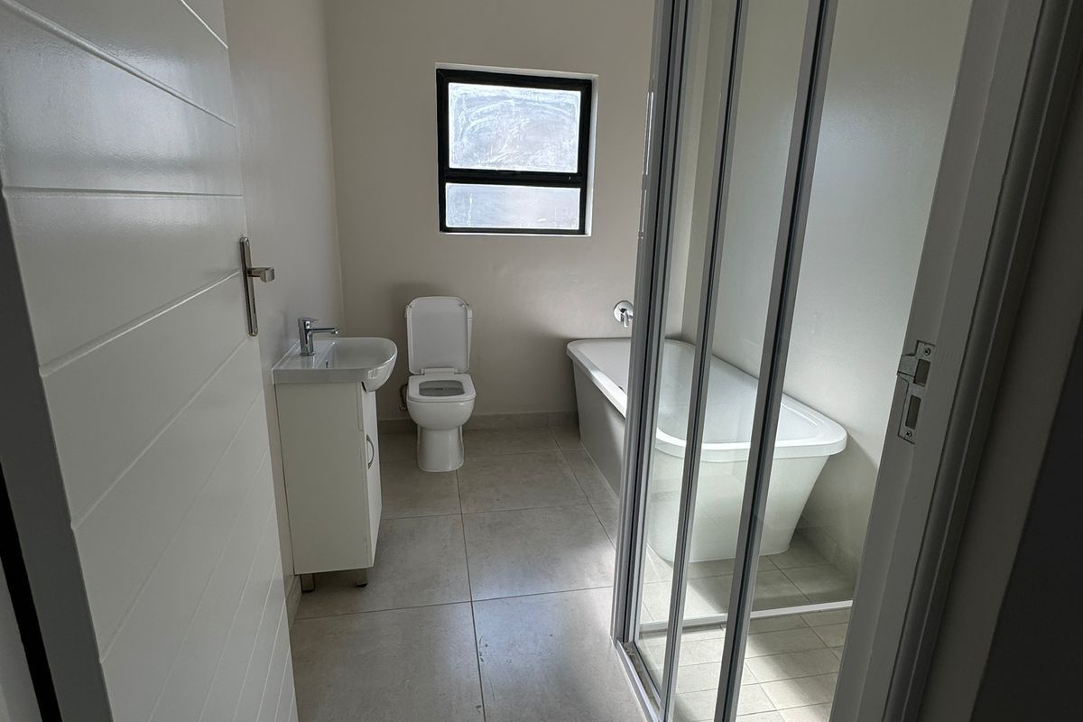 A clean, modern bathroom featuring a vanity with basin, toilet, bathtub, and a separate glass-enclosed shower with neutral floor tiling.