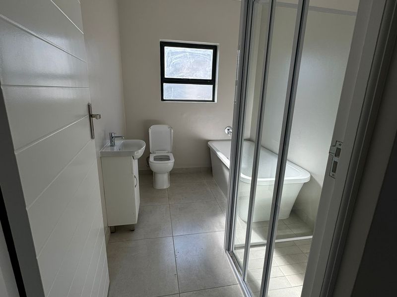 A clean, modern bathroom featuring a vanity with basin, toilet, bathtub, and a separate glass-enclosed shower with neutral floor tiling.